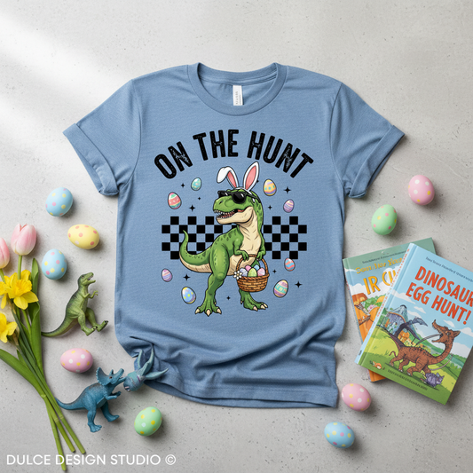 Blue t-shirt with dinosaur graphic and 'On the Hunt' text, surrounded by Easter decorations.