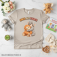 Beige t-shirt with monkey graphic and 'SMOL BUT FIERCE' text, surrounded by toys and decor on a light surface.