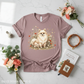 Mauve t-shirt with a dog and floral design on a marble surface with flowers and a book.