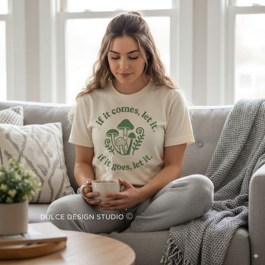 Woman sitting on a couch holding a mug, wearing a t-shirt with a design and text.