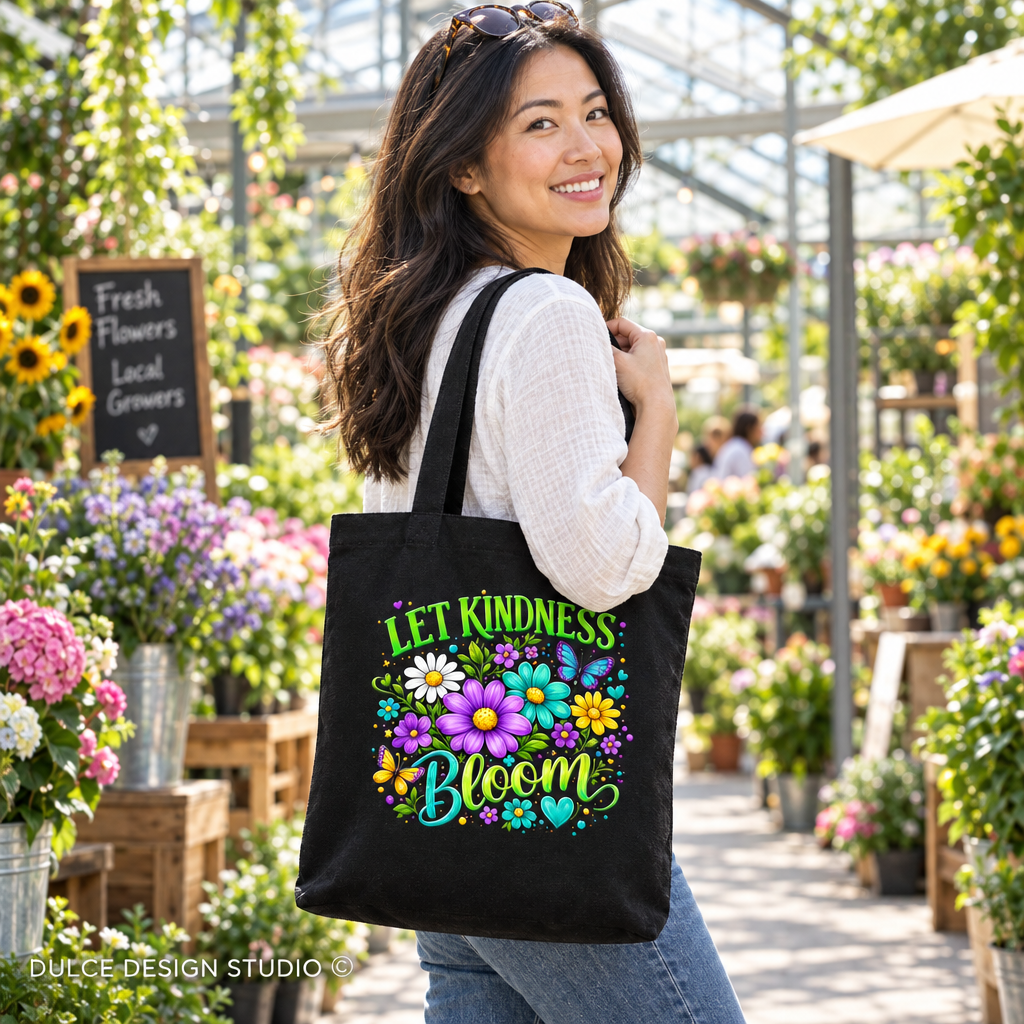 A woman in a flower shop wearing a white long-sleeve top and blue jeans carries a black canvas tote bag with a colorful floral design and the text 'LET KINDNESS BLOOM'.