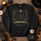 Black crewneck sweatshirt flat lay with vintage three witches under full moon design and Girls Will Be Girls banner