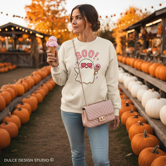 Woman wearing cream crewneck sweatshirt with drippy pink BOO text, ghost in heart sunglasses holding pink skull ice cream cone, at a pumpkin patch