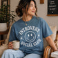 Woman wearing a blue 'Introvert Social Club' t-shirt holding a mug in a cozy room.