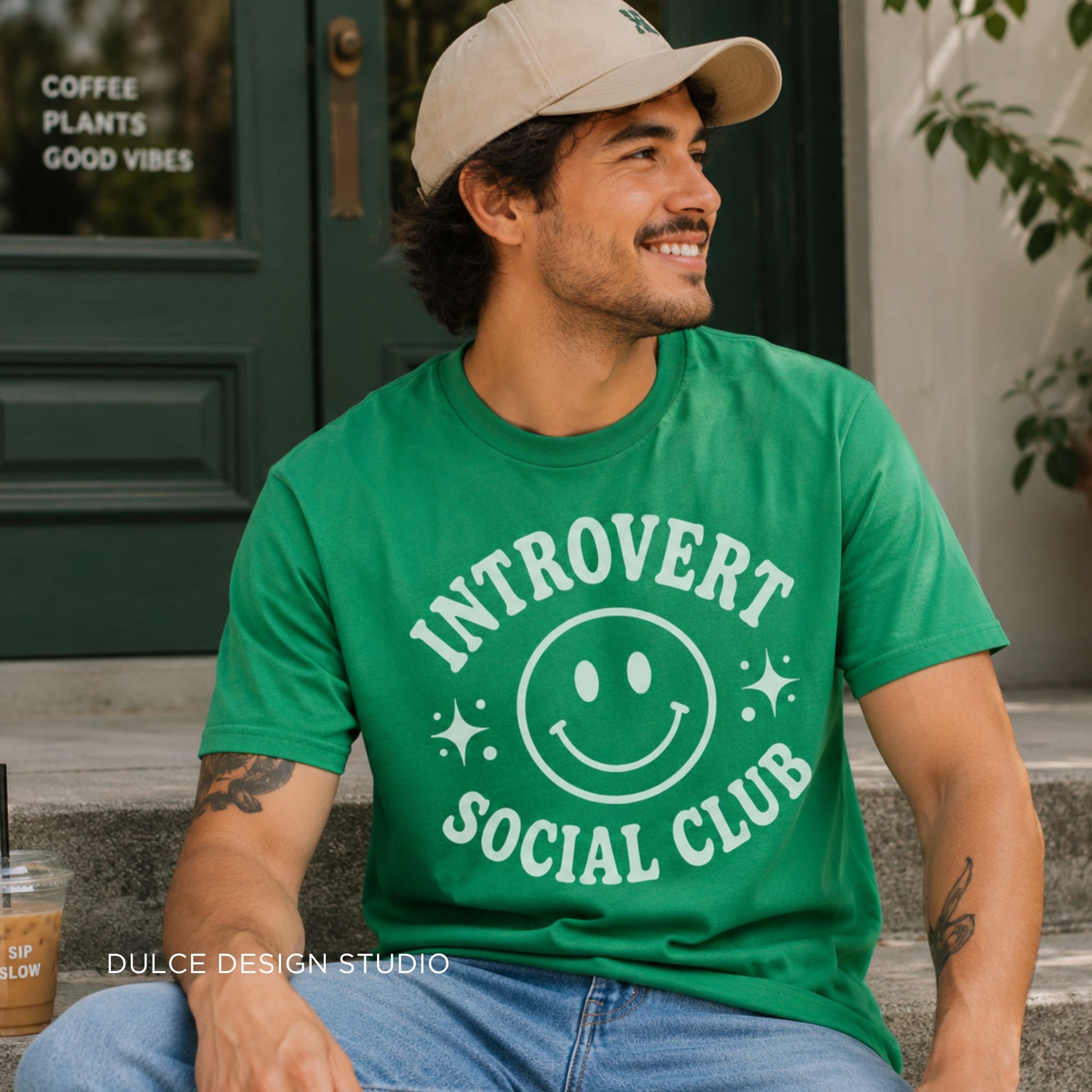 Man wearing a green t-shirt with 'Introvert Social Club' design, sitting outdoors.
