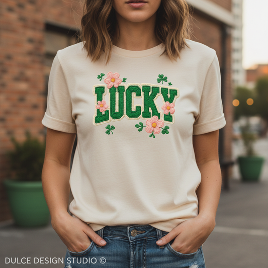 Person wearing a white t-shirt with 'LUCKY' and floral designs, standing outdoors.