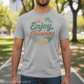 Person wearing a gray t-shirt with 'Enjoy the Journey' graphic in a park setting