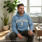 Man wearing a blue 'Jersey Made' hoodie sitting in a living room.