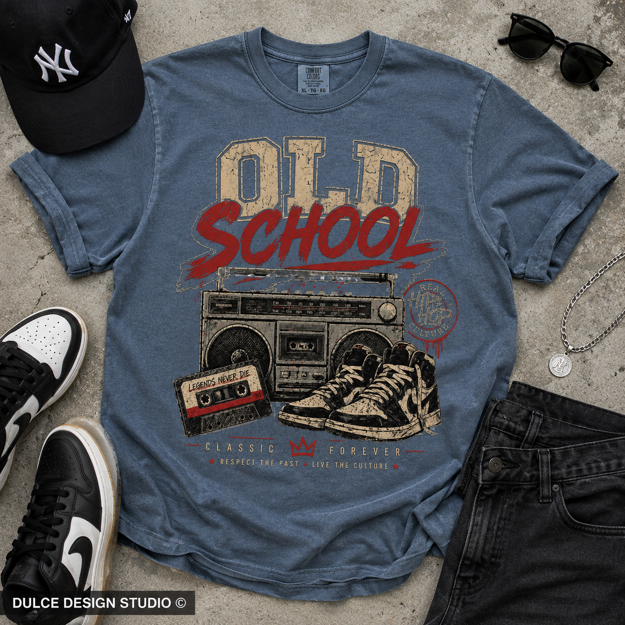 Blue t-shirt with 'Old School' graphic design on a concrete surface with sneakers and a cap.