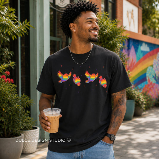 Man wearing a black t-shirt with colorful designs, holding a drink, standing in front of a building with a rainbow mural.