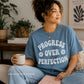 Person wearing a blue t-shirt with 'Progress Over Perfection' text, holding a mug and a book in a cozy room.