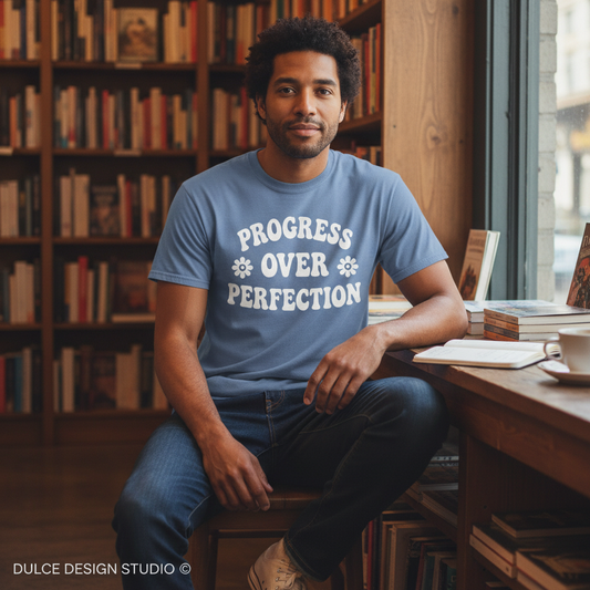 Man wearing a blue t-shirt with 'PROGRESS OVER PERFECTION' text in a cozy room with bookshelves.