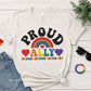Heather Natural-shirt with rainbow design and text on a wooden surface with accessories.