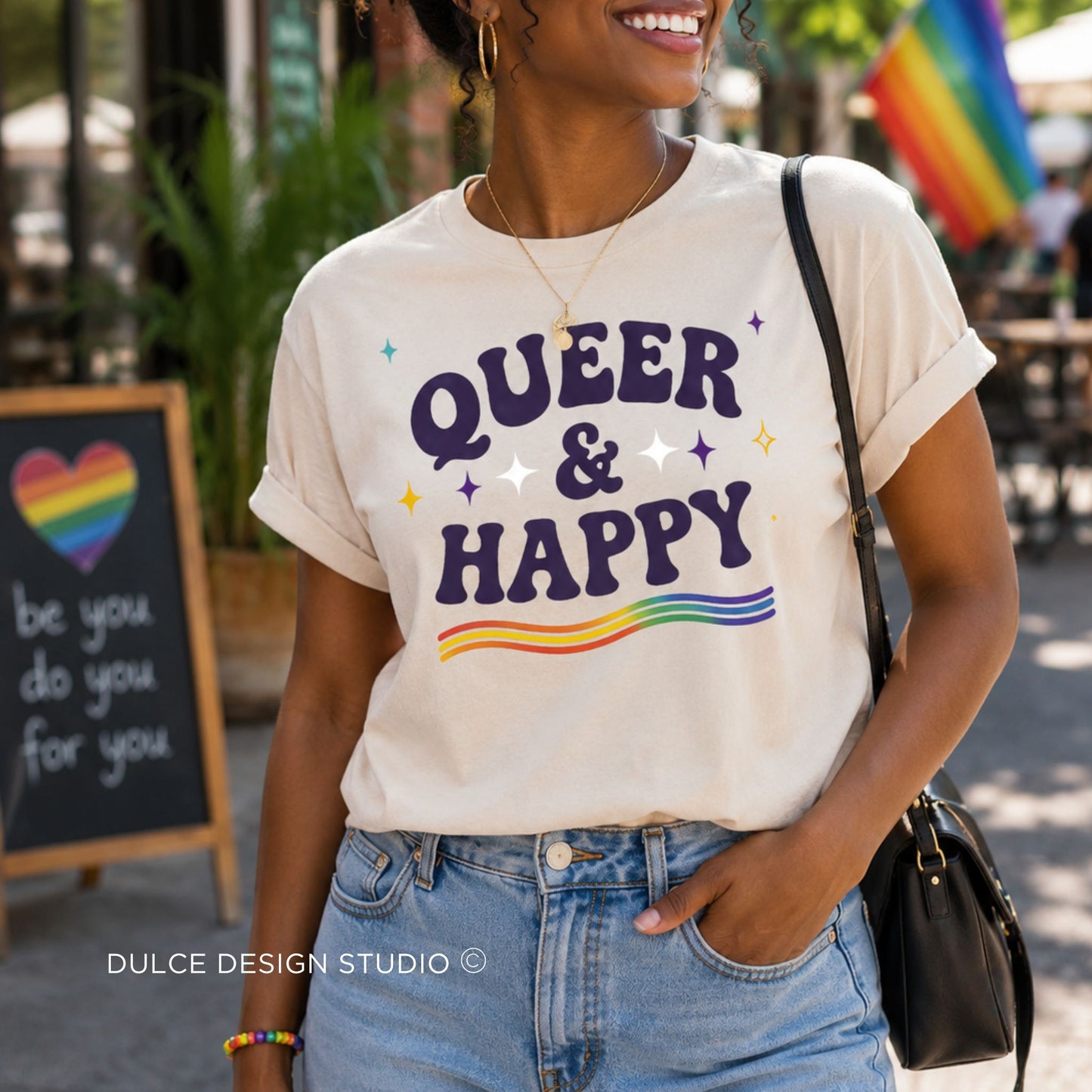 Person wearing a 'QUEER & HAPPY' t-shirt with rainbow elements in an outdoor setting.