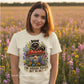 Woman wearing a t-shirt with a raccoon design and text in a field of flowers.