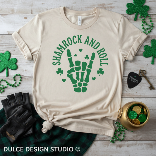 Beige t-shirt with green skeleton hand and shamrock design on a wooden surface with St. Patrick's Day decorations.