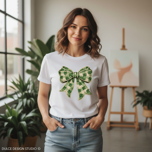 Woman wearing a white t-shirt with a green bow design in a room with plants and an easel.