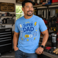 Man wearing a blue t-shirt with 'Super Dad Mode' design in a workshop.