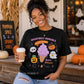 A woman wearing a black graphic t-shirt with a cute Halloween ice cream design, holding a coffee cup in a fall-themed storefront setting.