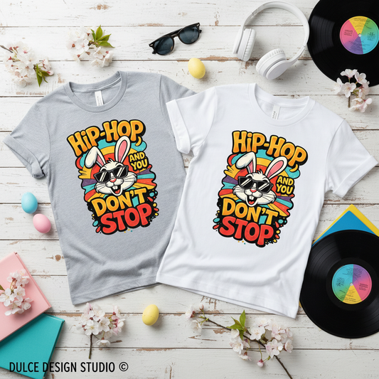 Two t-shirts with a colorful graphic design featuring text and a rabbit illustration on a wooden surface with decorative items.