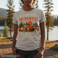 Person wearing a t-shirt with a camping graphic and text in a natural setting.