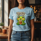 Person wearing a light blue t-shirt with a frog and coffee design, standing in a cozy indoor setting.