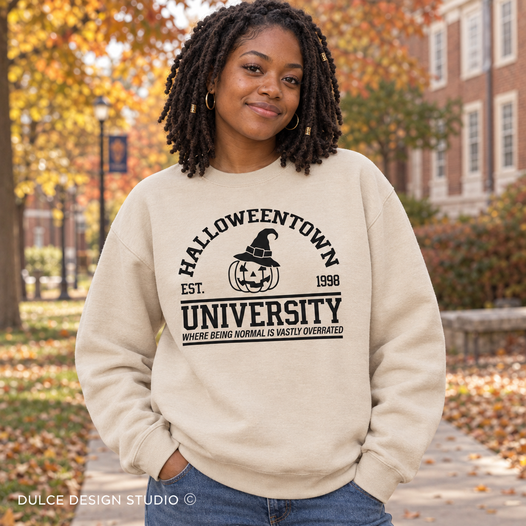 Woman on a fall campus wearing a sand Halloweentown University Halloween crewneck sweatshirt.