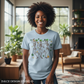 Woman wearing heather ice blue t-shirt with dancing skeletons design