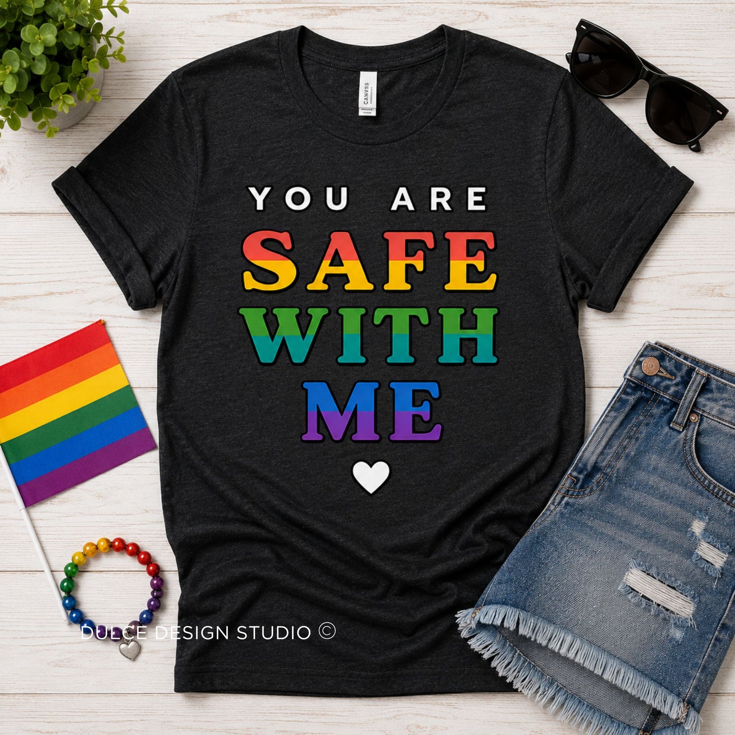Heather Black t-shirt with 'You are safe with me' text in rainbow colors, surrounded by accessories on a wooden surface.