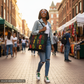 Woman walking on a street market holding a colorful tote bag with text.