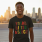 Man wearing a black t-shirt with 'YOUNG, GIFTED & BLACK' in colorful letters, standing against a city skyline.
